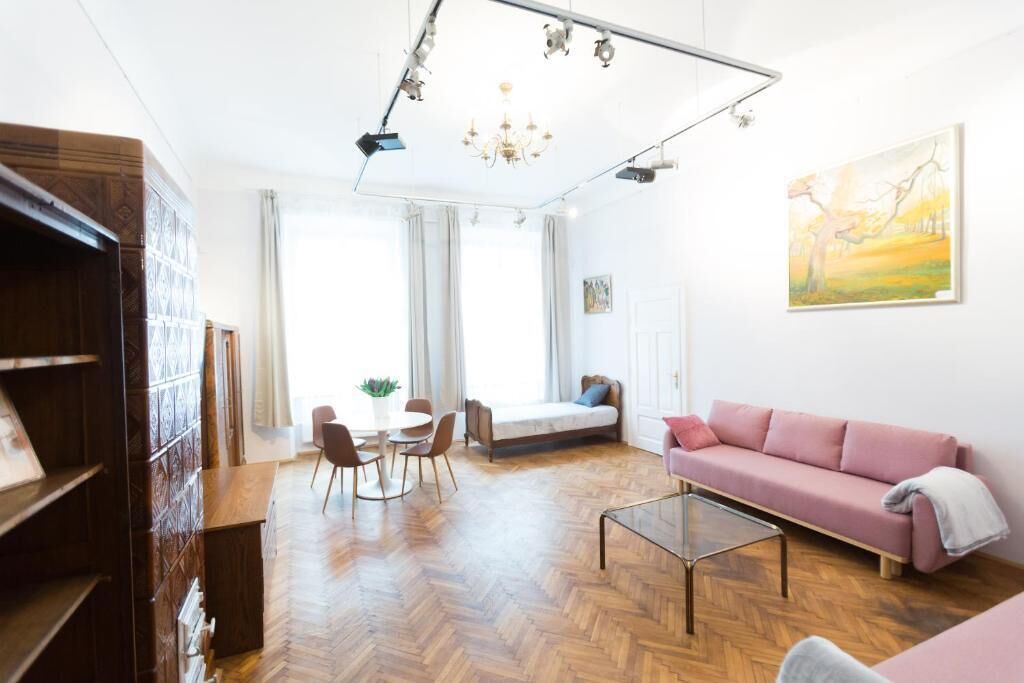 A modern living room with a herringbone floor, a pink sofa, a glass coffee table, and a dining area with chairs and a table.