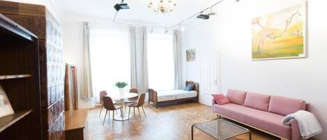 A modern living room with a herringbone floor, a pink sofa, a glass coffee table, and a dining area with chairs and a table.
