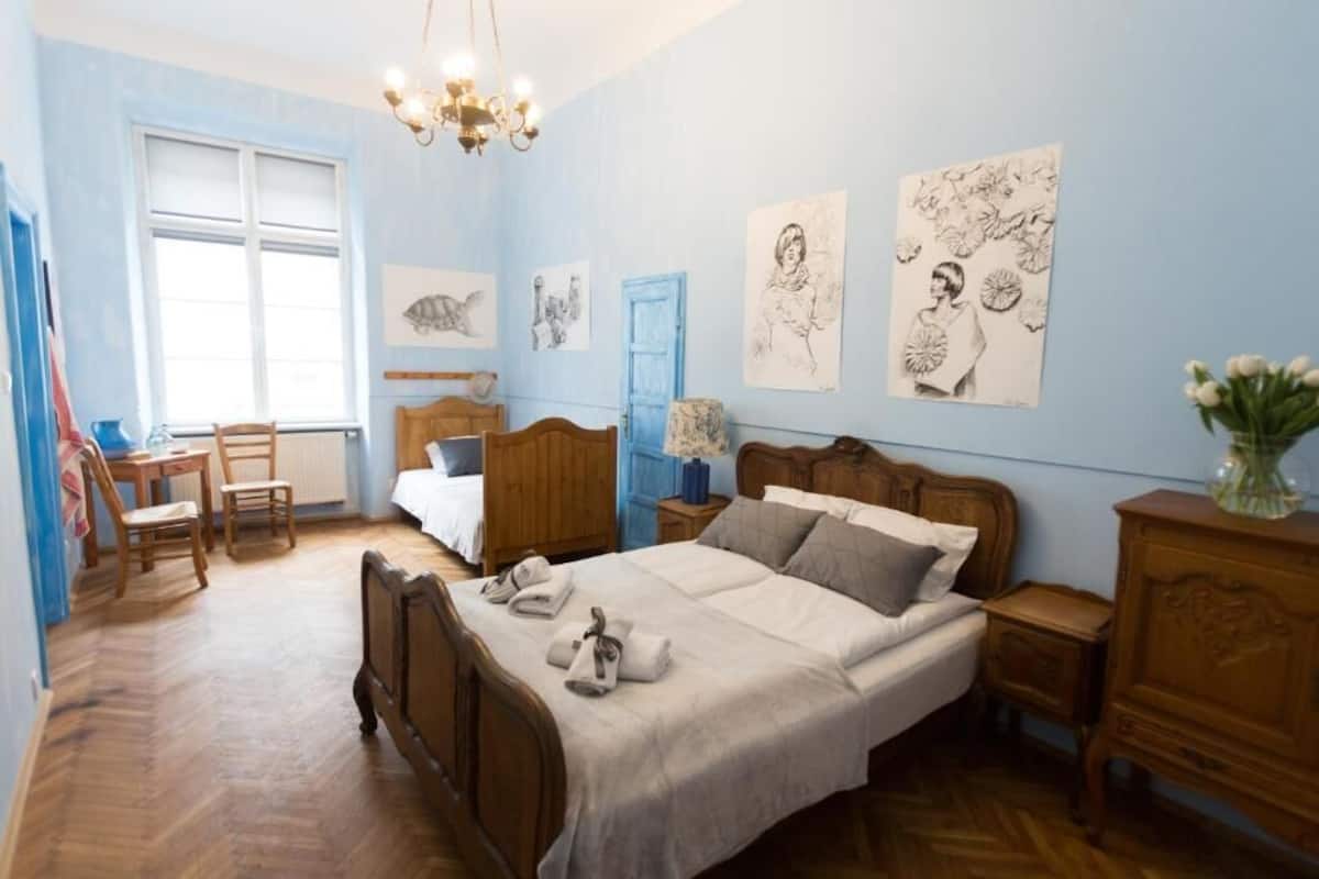 A bedroom with a wooden bed, a desk, and chairs. There are wall art pieces and a chandelier.