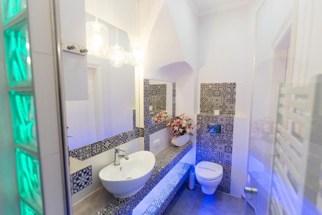 A bathroom with a white sink, a toilet, and a mirror. There is a decorative vase with flowers on the counter.