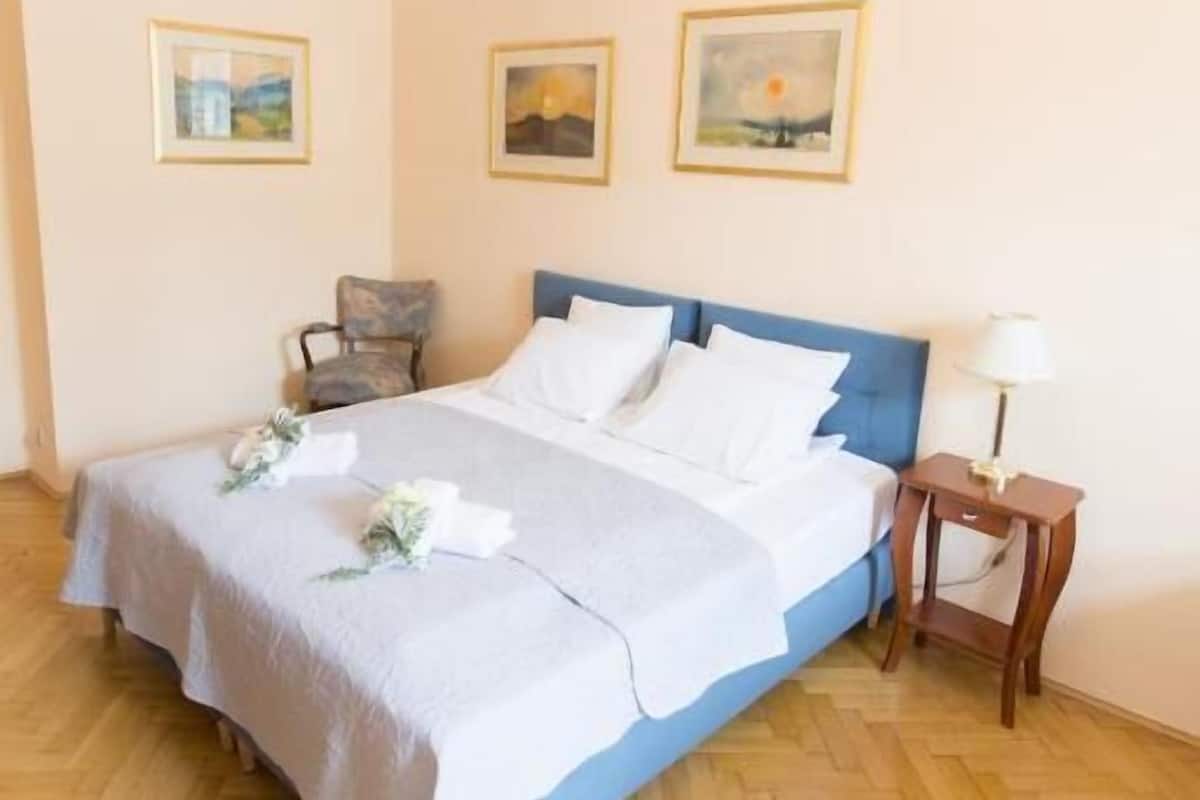 A bedroom with a bed, a chair, a nightstand, and a chandelier.