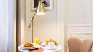 A small round table with a white tablecloth, a gold floor lamp, a chair, and a breakfast setting including croissants, a cup, and a glass of orange juice. - Roman Apartments (Kraków)