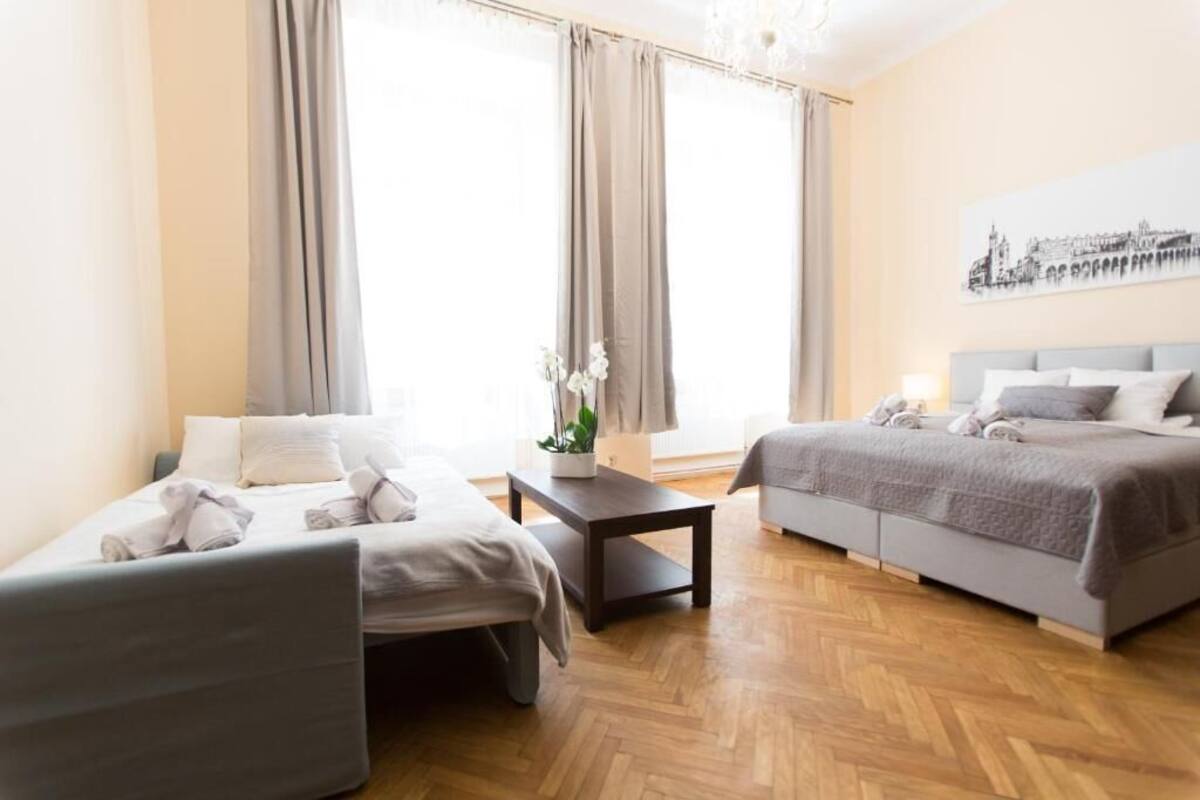 A hotel room with two beds, a small table with a plant, and a large window with curtains.