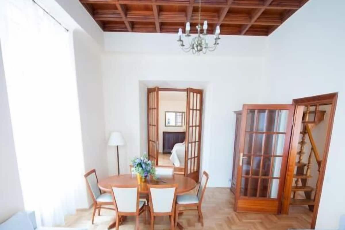 A spacious living area with a wooden ceiling, a glass coffee table, and a dining table with chairs.