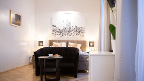 A bedroom with a bed, bedside tables, a small table with a cup and a pastry, and a wall-mounted picture. - Roman Apartments (Kraków)
