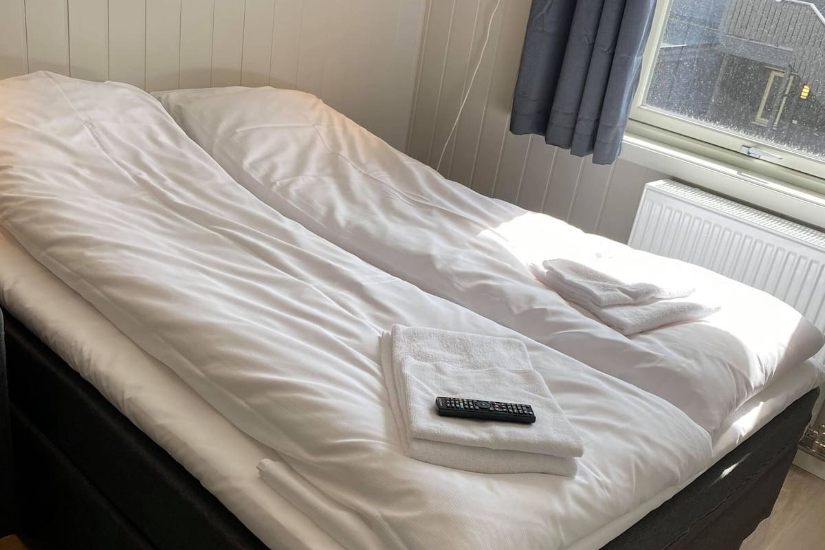 Una cama bien hecha con ropa de cama blanca, un control remoto y una toalla sobre la cama.