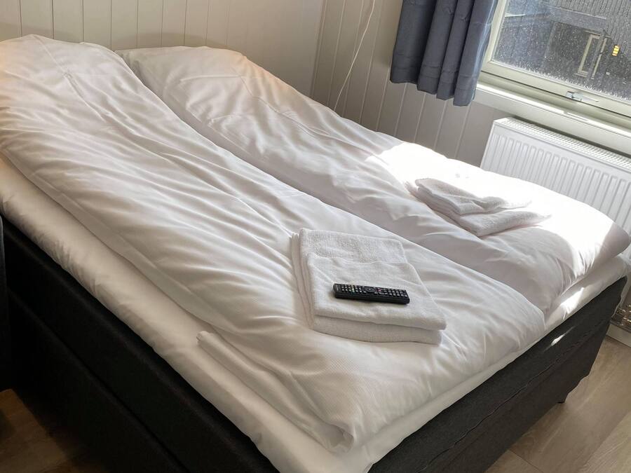 Un lit bien fait, avec du linge de lit blanc, une télécommande et une serviette posée sur le lit.