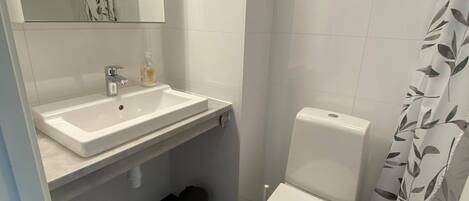 A bathroom with a white sink, mirror, toilet, and shower curtain.