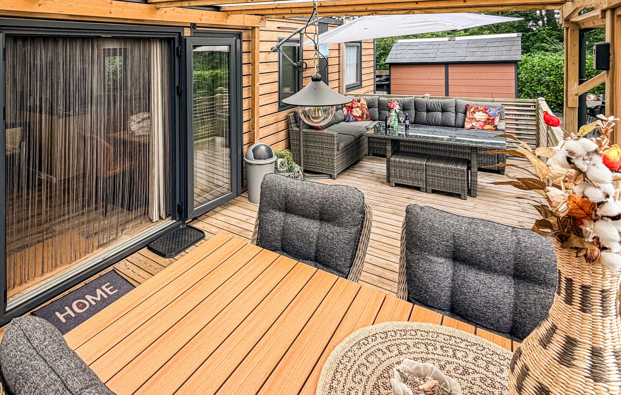 A covered outdoor seating area with a wooden deck, a sliding glass door, and a wicker sofa set.