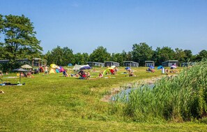 Um camping com tendas, um campo gramado e uma pequena área de água.