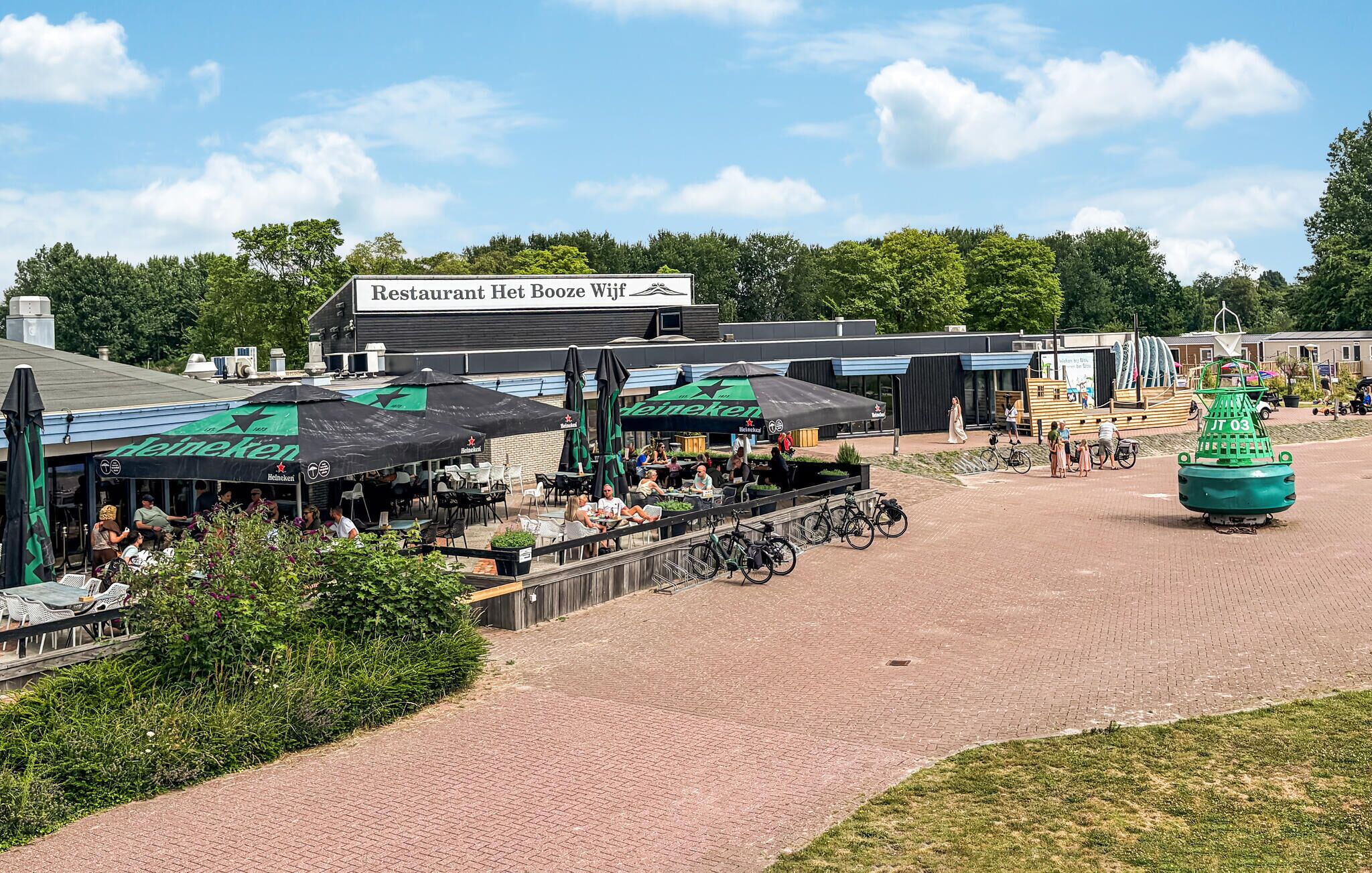 Un restaurant appelé « Restaurant Het Boze Wijf » qui dispose d’une terrasse et de parasols à l’effigie de la marque « Heineken ».