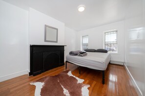 Un dormitorio con chimenea, una cama con almohadas, un tapete de piel de vaca y dos ventanas.