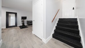 Un interior moderno con una escalera, paredes blancas y un suelo de baldosas grises.