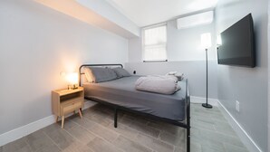 Un dormitorio moderno con cama, mesita de noche, lámpara y televisor montado en la pared.
