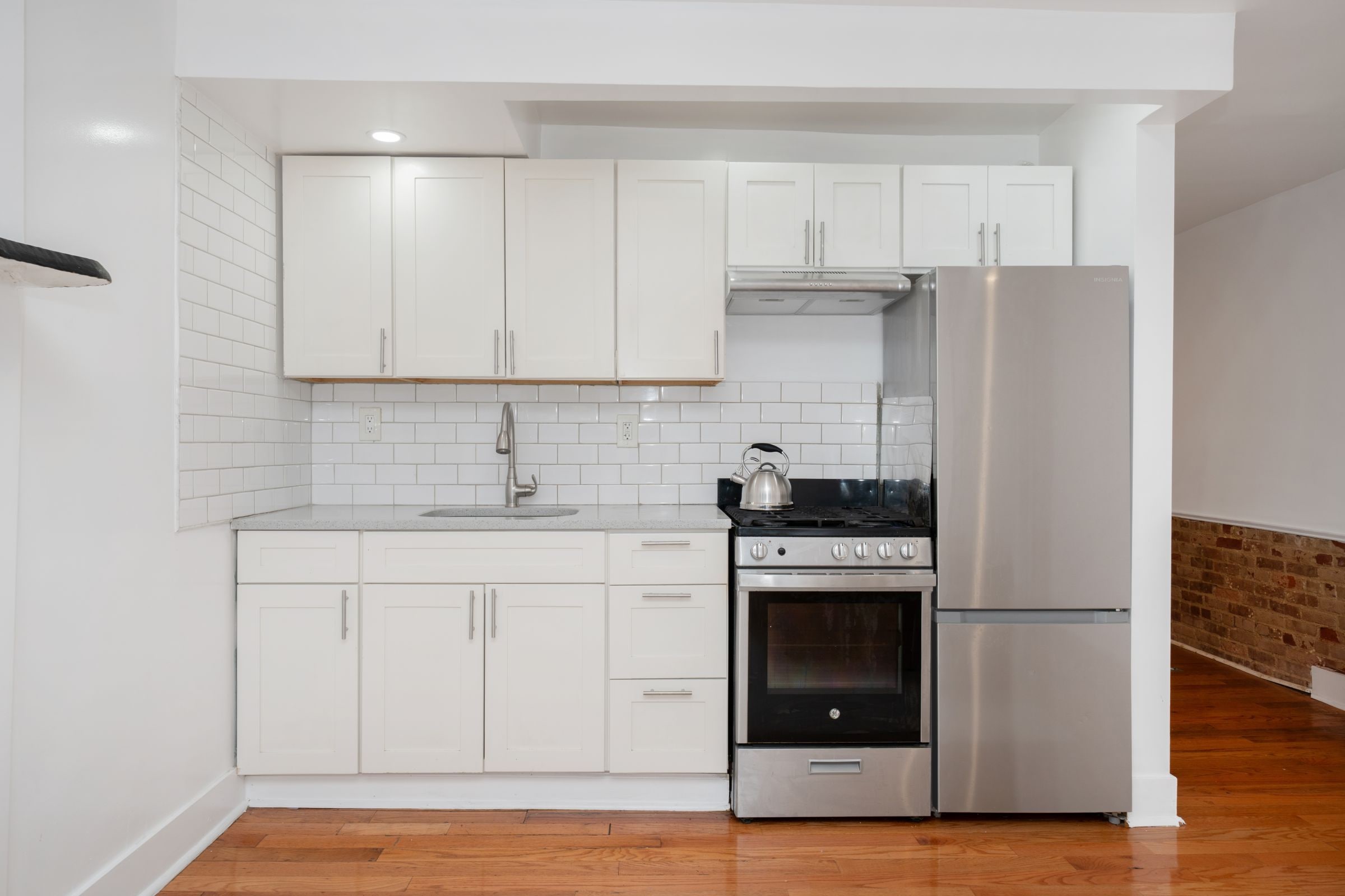 Une cuisine compacte avec des meubles blancs, un réfrigérateur en acier inoxydable, une cuisinière à gaz et un four encastré.
