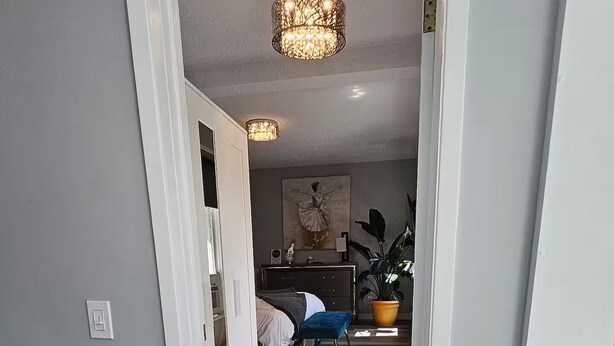 Un pasillo que conduce a un dormitorio con cama, mesita de noche y planta en maceta.