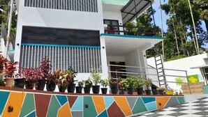 A modern two-story building with a balcony, surrounded by potted plants and a colorful geometric wall. - VGK RESIDENCY Premium Serviced Apartments (KL)