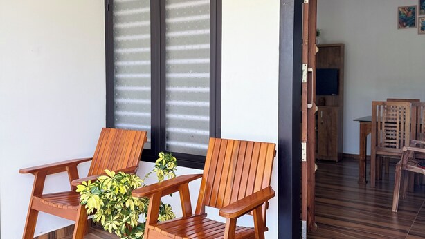 A room with two wooden chairs, a small table, and a potted plant. There is a door labeled "KARLAD A1" leading to another room with a dining table and chairs. - VGK RESIDENCY Premium Serviced Apartments (KL)