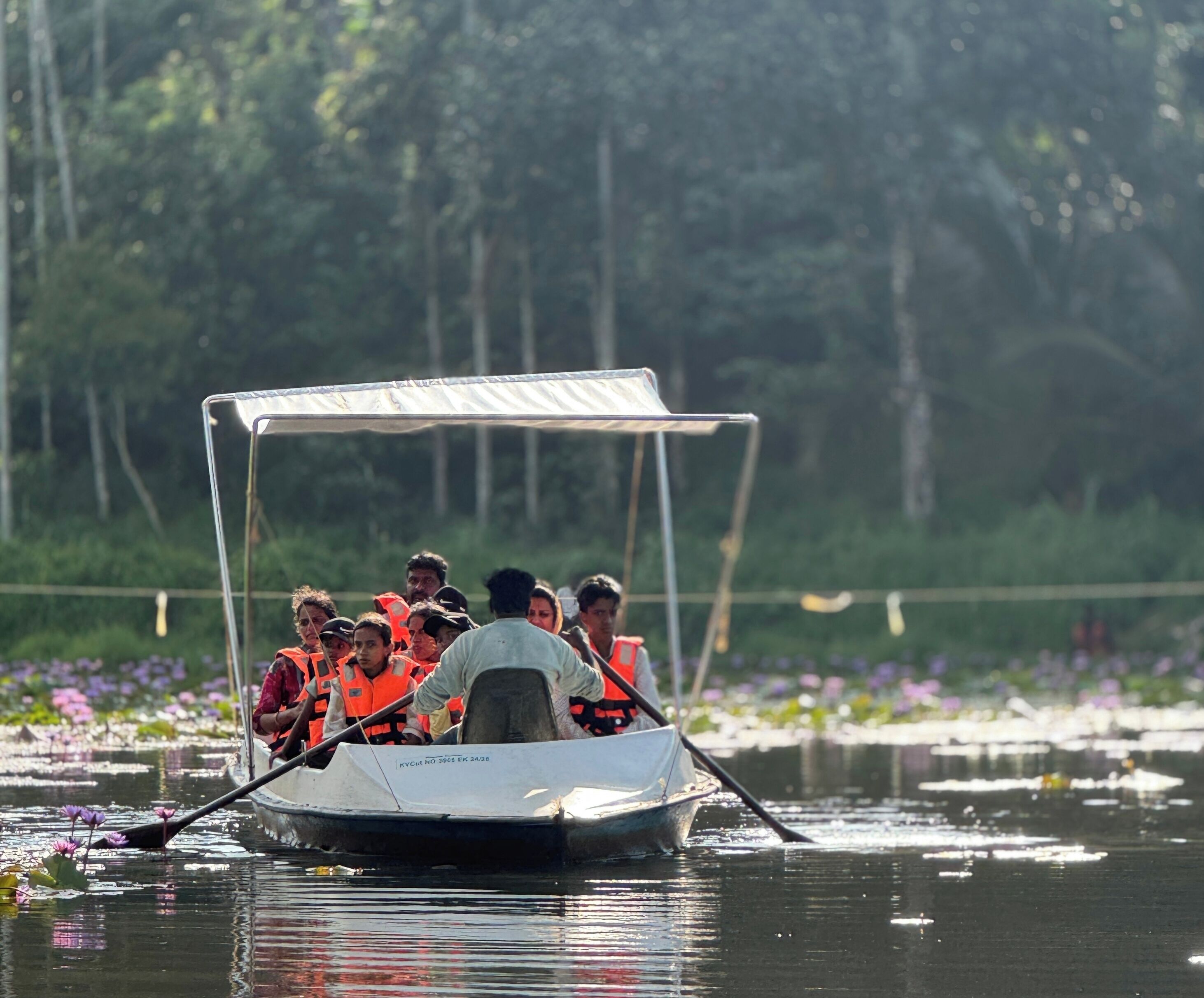 A boat with passengers wearing life jackets on a calm body of water surrounded by greenery.