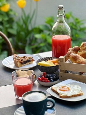 Een ontbijttafel met diverse lekkernijen, waaronder toast met ei, een glas sap, een schaal bessen, een plakje taart, een fles sap en een mand croissants.