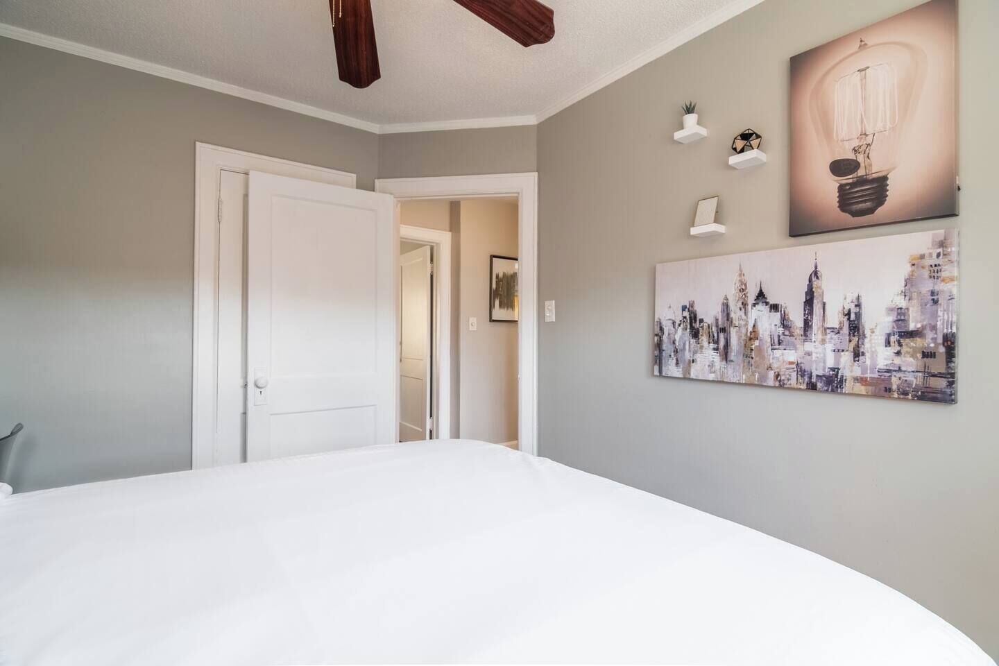 A bedroom with a large bed, a cityscape painting, and a light bulb artwork on the wall.