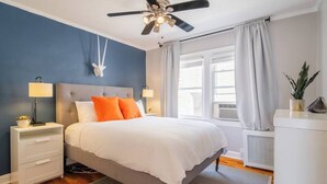 A bedroom with a bed, nightstands, a ceiling fan, a window with curtains, and a radiator.