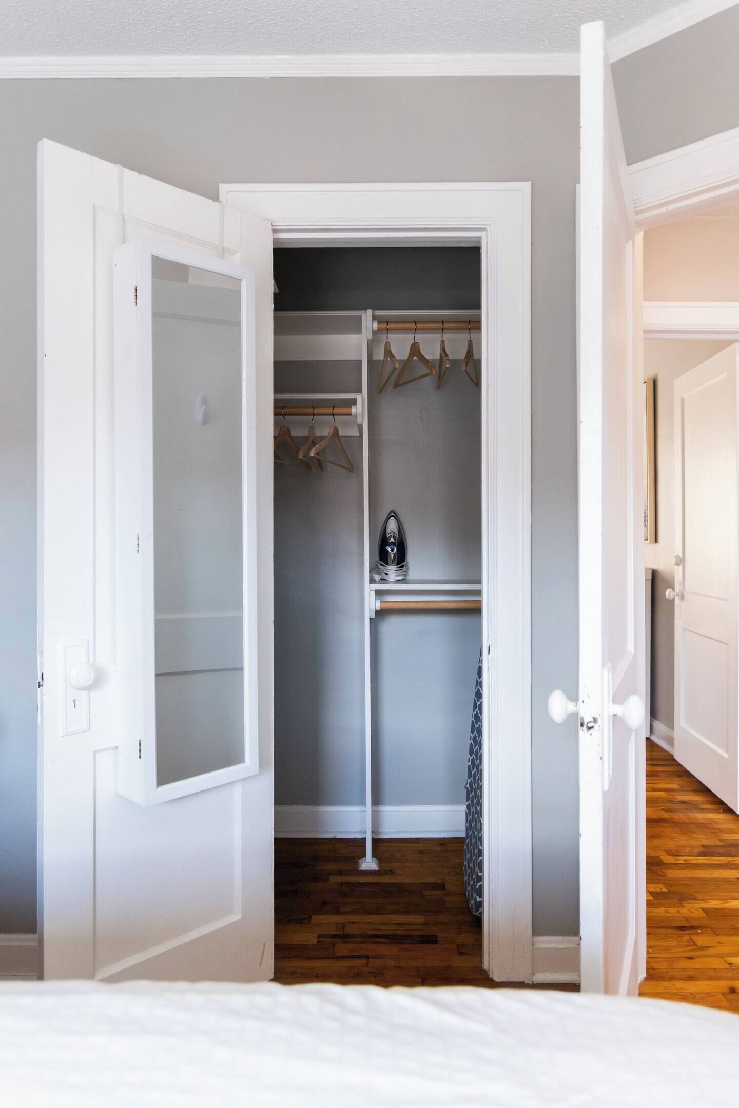 Una habitación con una cama, un armario con ropa colgada y un zapatero.