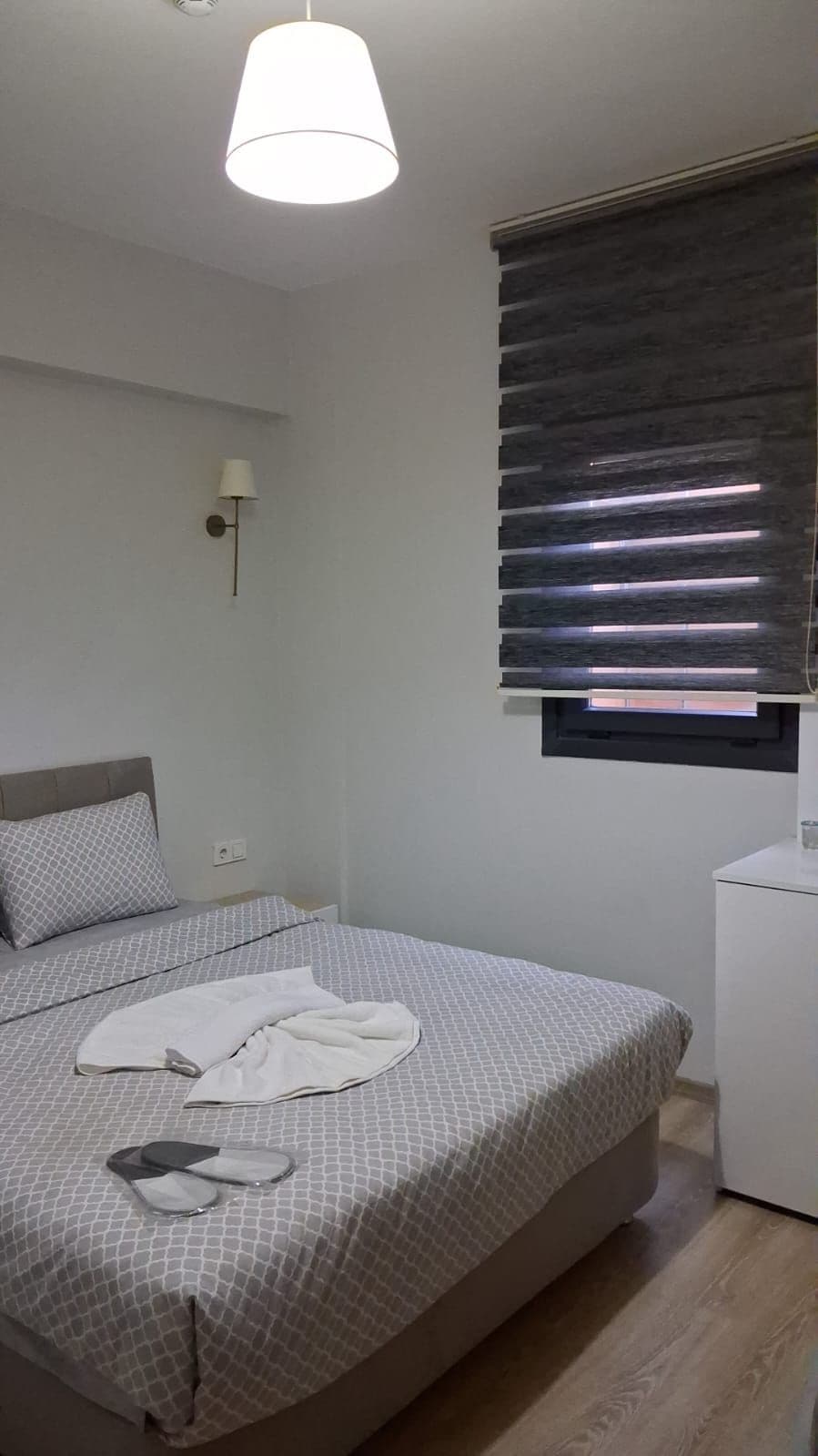 Un dormitorio con cama, mesita de noche, lámpara y ventana con persianas.