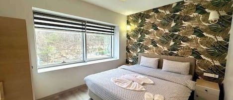 A bedroom with a large window, a bed with a patterned bedspread, and a wall with a leaf pattern.