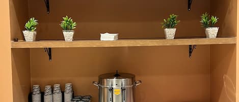 A kitchenette with a coffee maker, tea pots, and a food warmer.