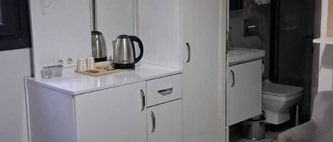 A hotel room with a bed, a desk with a kettle, a wardrobe, a bathroom with a toilet, and an air conditioning unit.