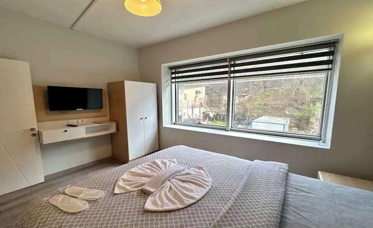 A bedroom with a bed, a television mounted on the wall, and a window with blinds.