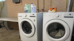 Two front-loading LG washing machines in a laundry room with a bench and cleaning supplies on top.