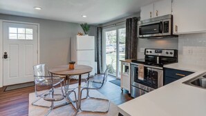 A modern kitchen with white cabinets, stainless steel appliances, and a dining area with clear chairs and a wooden table.