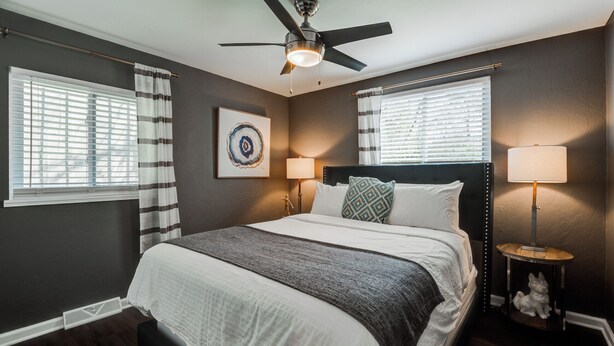 A bedroom with a bed, two bedside lamps, a ceiling fan, and a window with blinds.