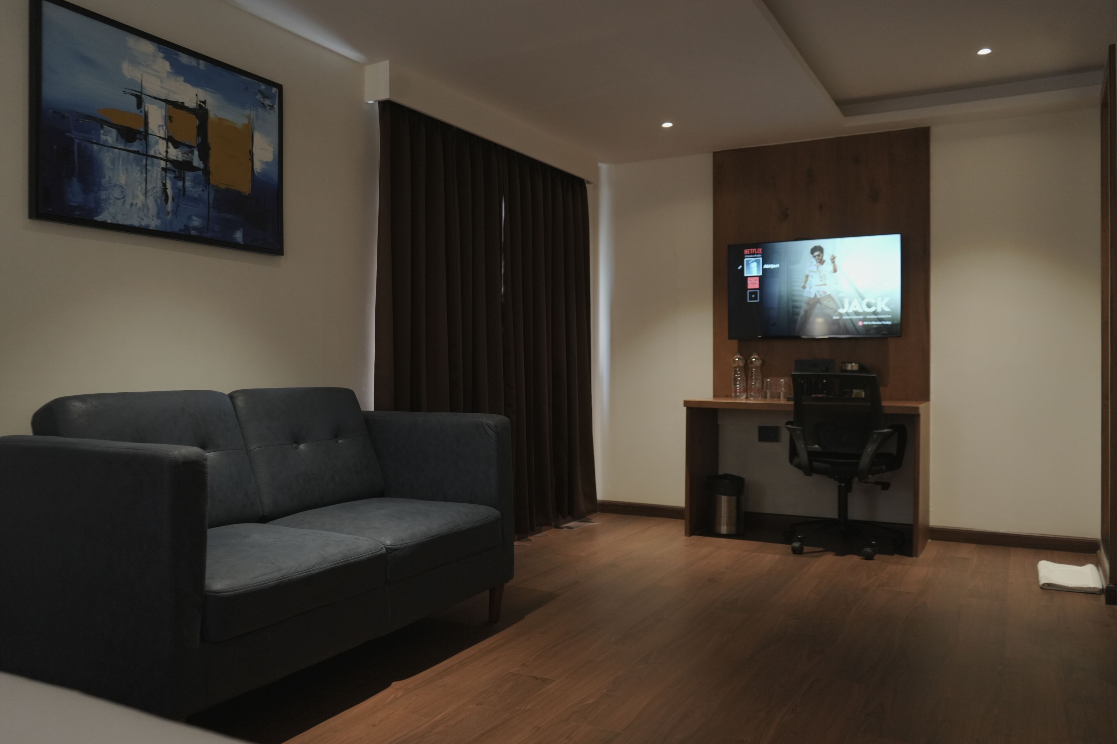 A modern living room with a grey sofa, a wooden desk, and a mounted TV displaying a movie poster.