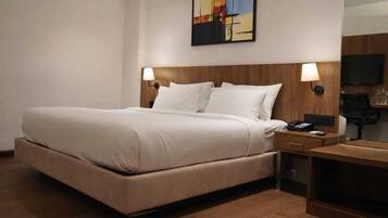 A hotel room with a large bed, two bedside tables, a desk, a chair, a TV, and a painting on the wall.