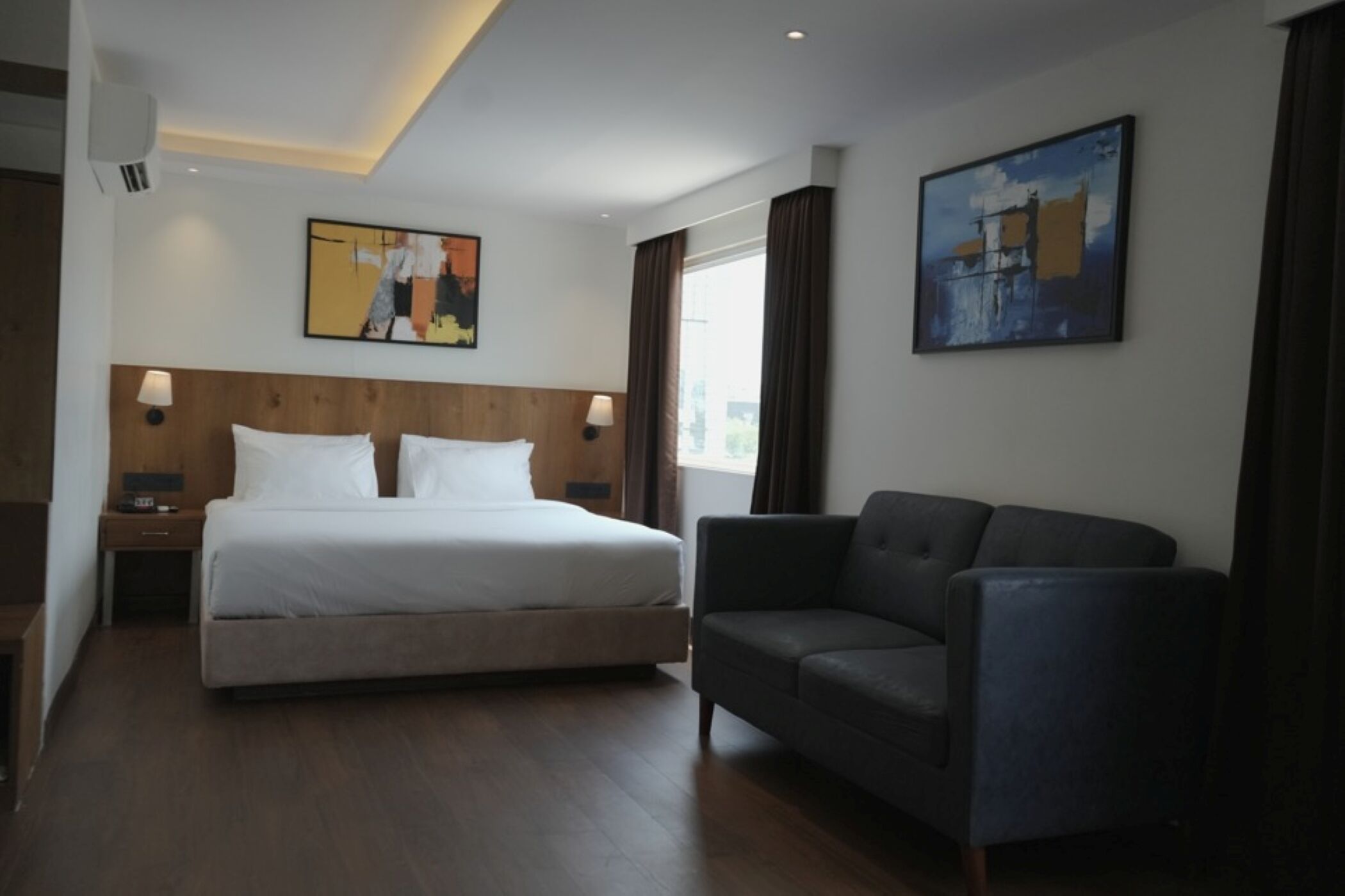 A hotel room with a large bed, a dark armchair, and two paintings on the walls.
