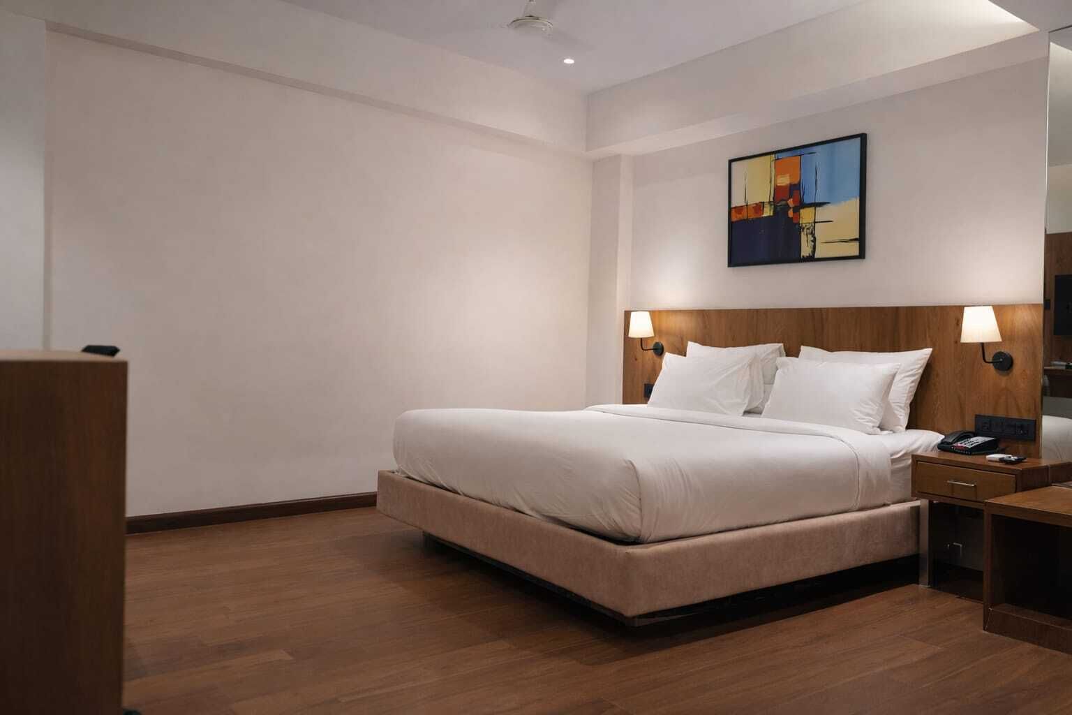 A hotel room with a bed, bedside lamps, a nightstand, a wooden headboard, and a painting on the wall.