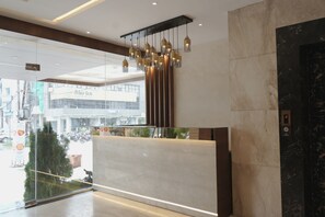A modern reception area with a marble reception desk, a glass wall with a view of the street, and a decorative hanging light fixture. - Silvotel By Bizzgrow Hotels (Indore)