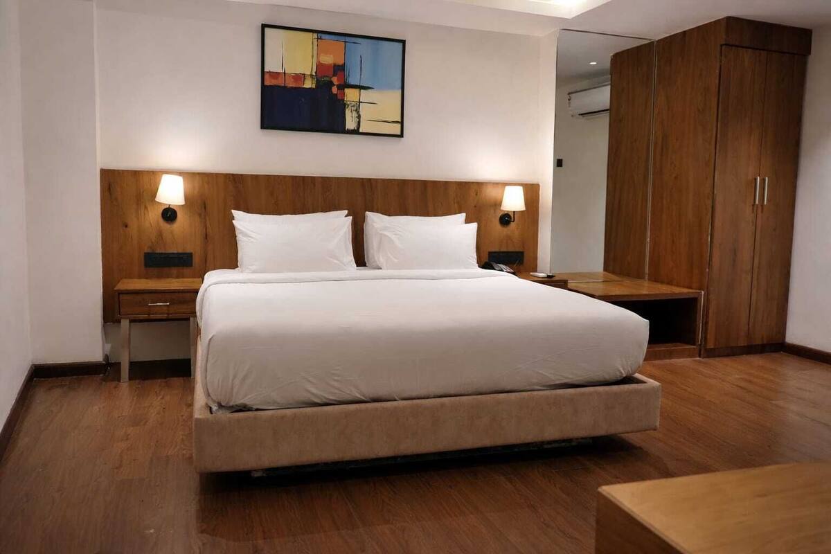 Ein Hotelzimmer mit einem großen Bett, einem Holzkopfstück, Nachttischen mit Lampen, einem Schrank aus Holz und einem Gemälde an der Wand.