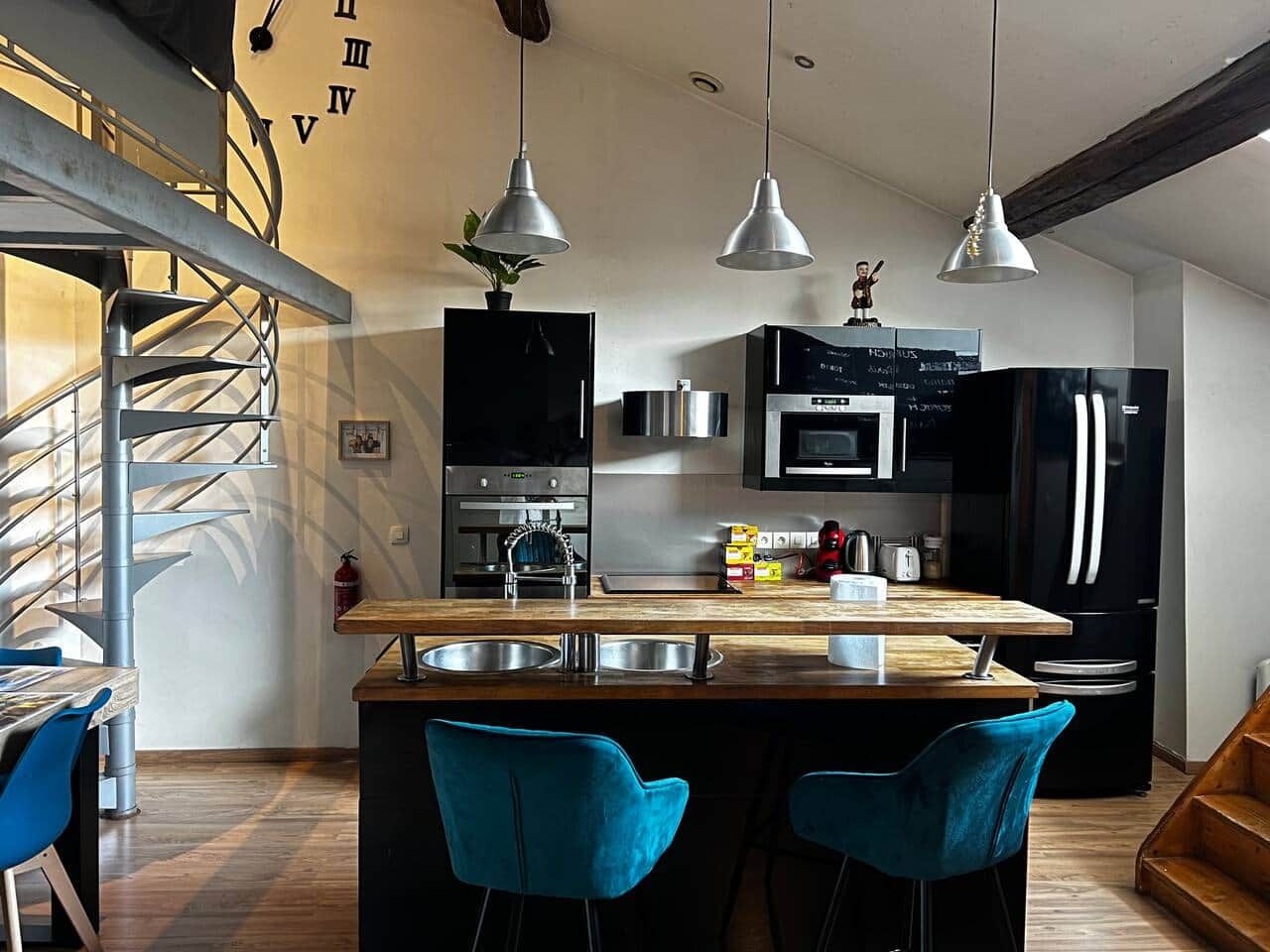 Une cuisine moderne dotée d’un îlot central, d’appareils électroménagers en acier inoxydable et de chaises bleues.