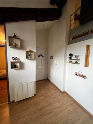 A narrow hallway with wooden flooring, white walls, and a white door at the end. Shelves with various items are mounted on the walls. - Rare gem located in the beating heart of Old Lyon. (Lyon)