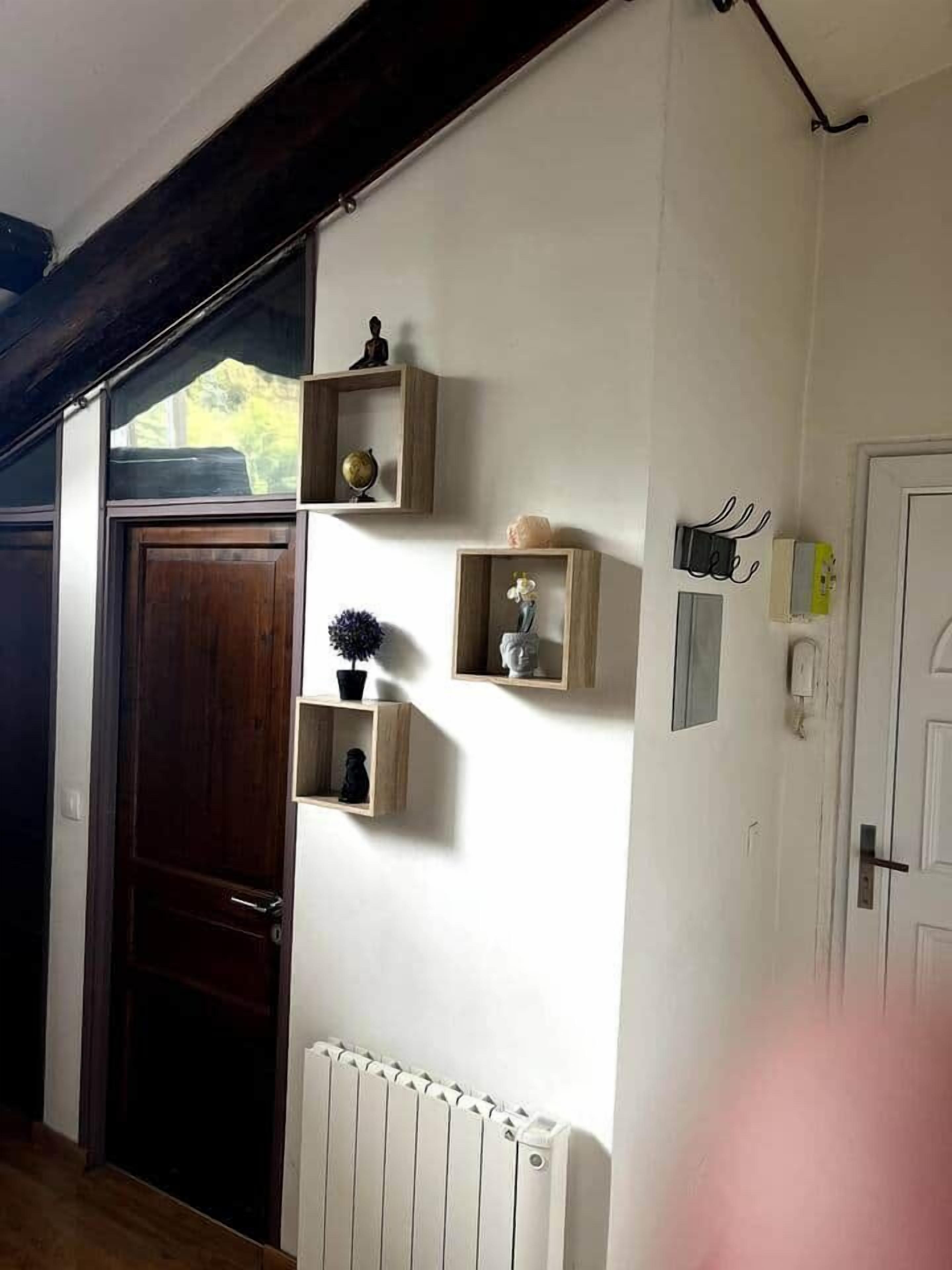 Une pièce avec une porte en bois, un radiateur blanc et des étagères murales ornées d’objets décoratifs.