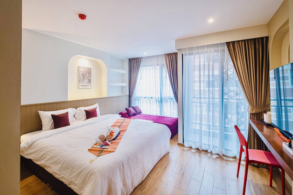 Une chambre d’hôtel avec un grand lit, un bureau et une chaise. Il y a une fenêtre avec des rideaux et une vue sur l’extérieur.
