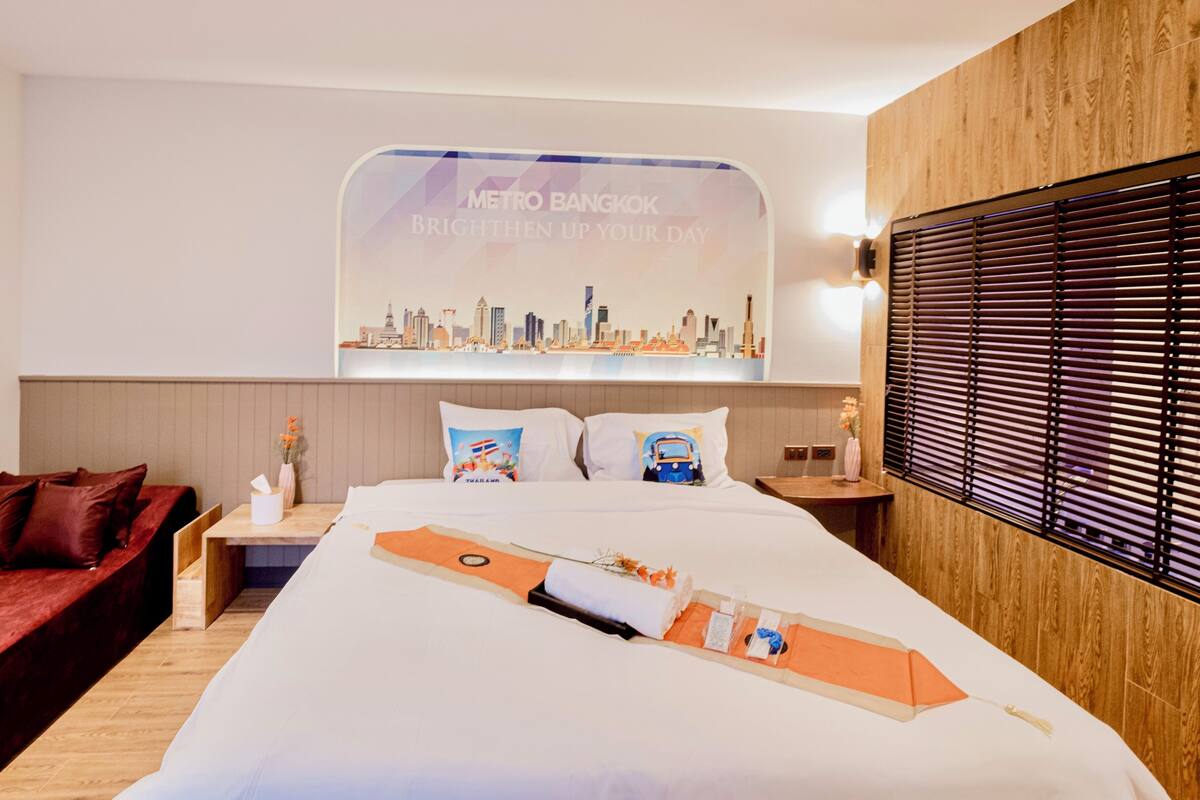 Une chambre d’hôtel avec un grand lit, une affiche représentant un paysage urbain accrochée au mur, une tête de lit en bois et un canapé rouge.