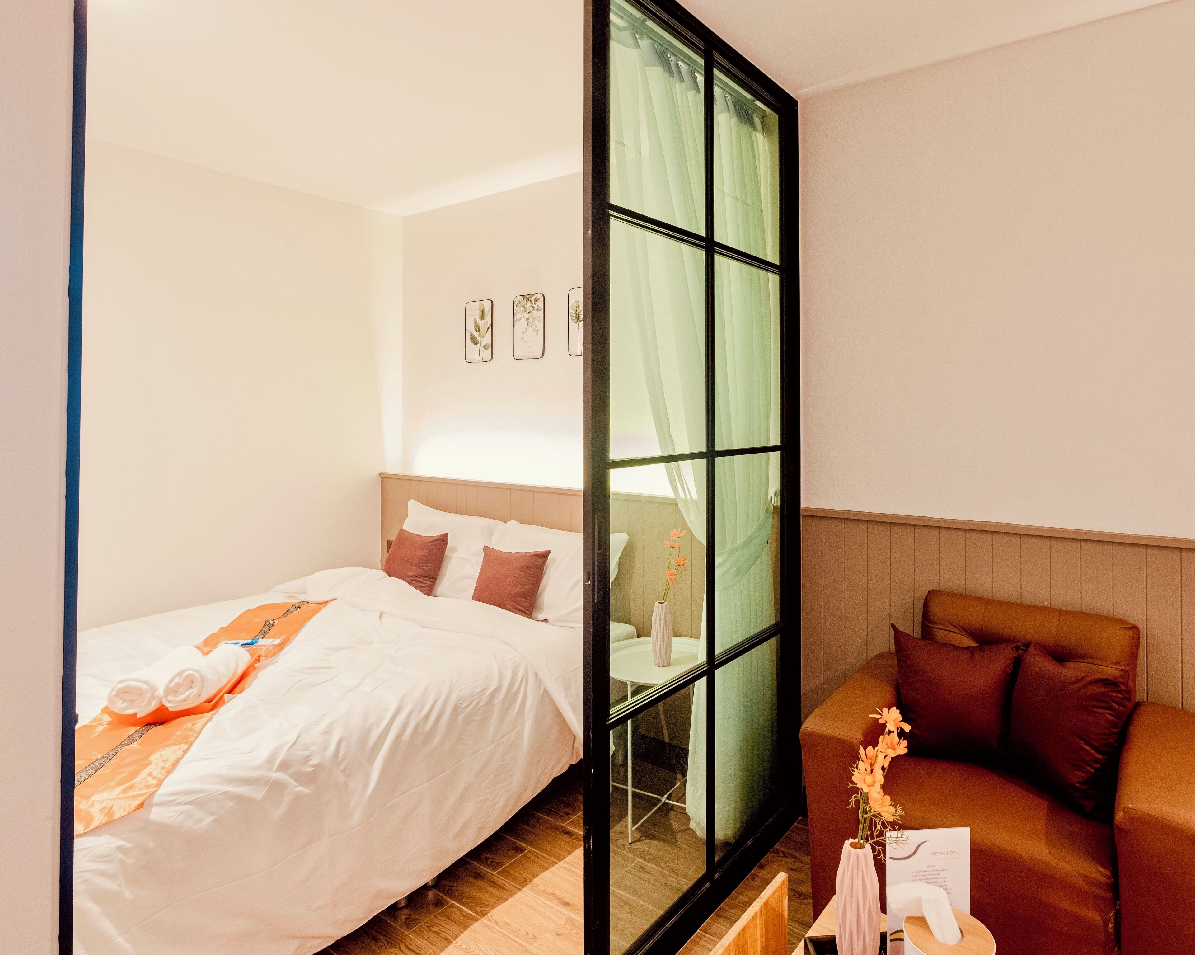 Habitación de hotel con cama, sofá, una mesita con un jarrón y una ventana con cortinas.
