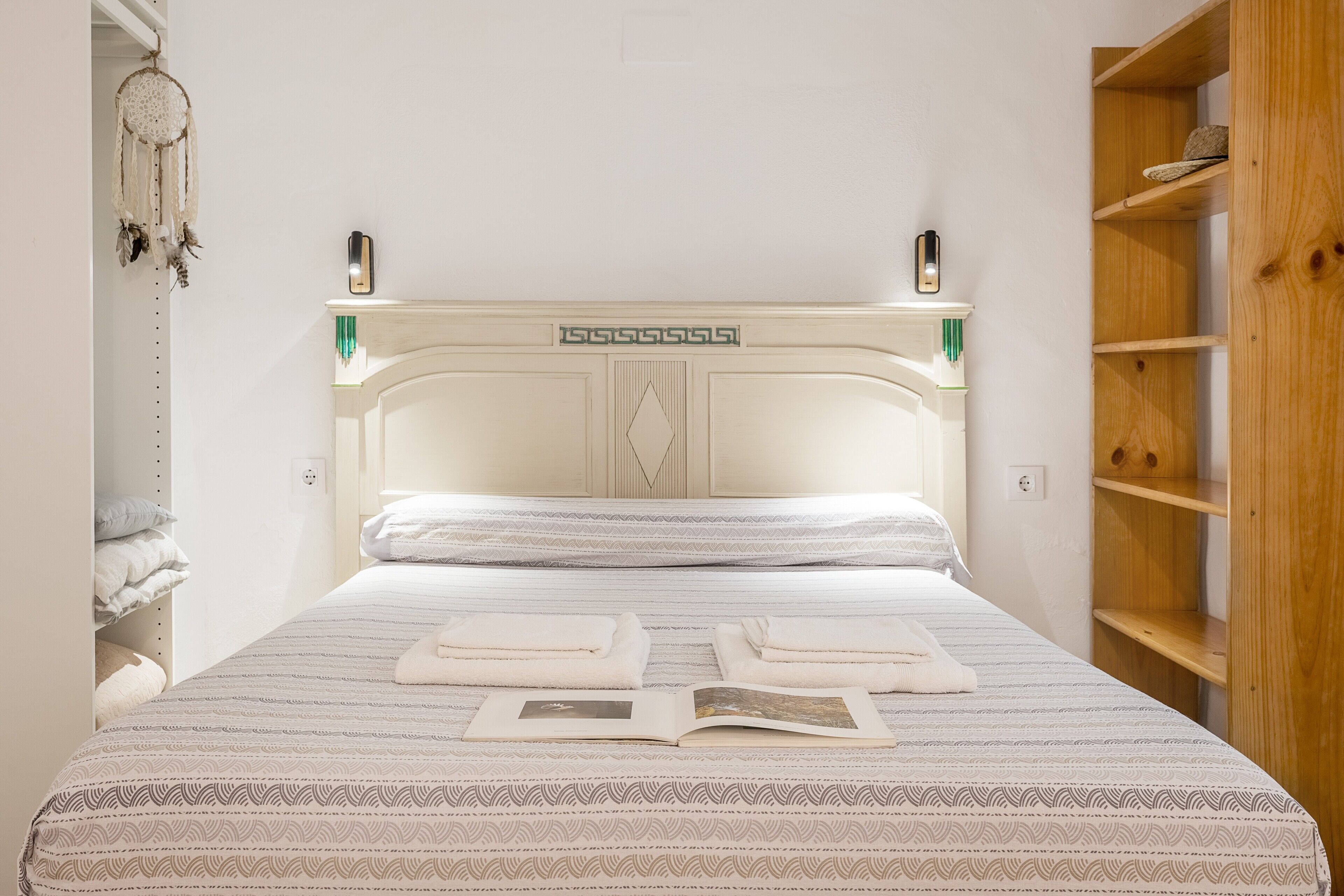 A neatly made bed with a patterned bedspread, a bedside table with a lamp, and a dreamcatcher hanging on the wall.