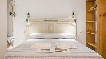A neatly made bed with a patterned bedspread, a bedside table with a lamp, and a dreamcatcher hanging on the wall.