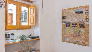 Quarto com um armário de madeira, um mapa na parede, uma planta e uma estante com livros e um telefone.